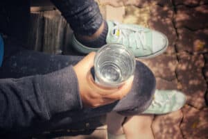Bird's eye view of woman holding a clear glass of water on her knee with her teal Converse shoes in the shot.
